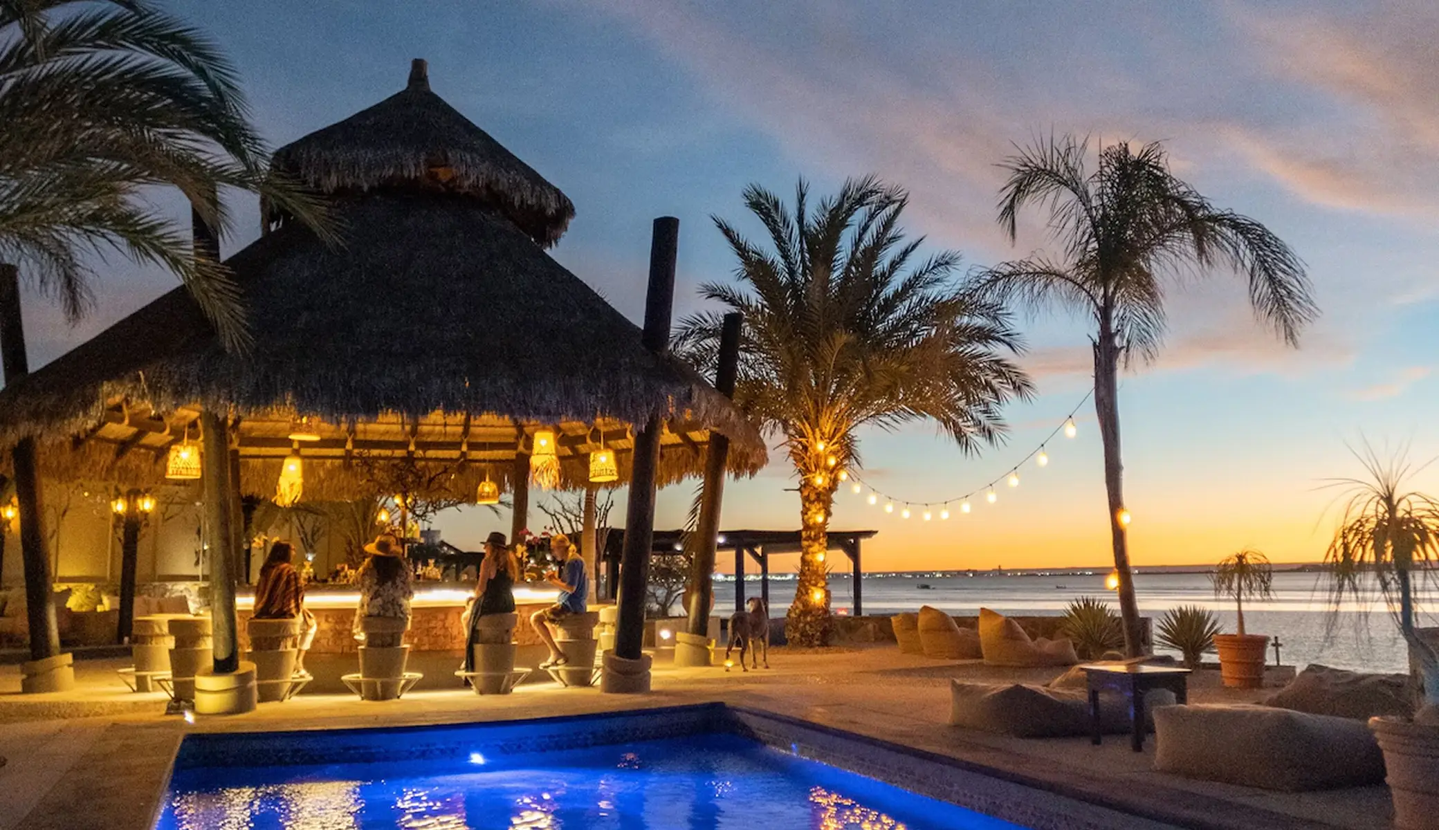 El Caimancito's palapa bar at dusk, with guests seated and the pool facing the sea