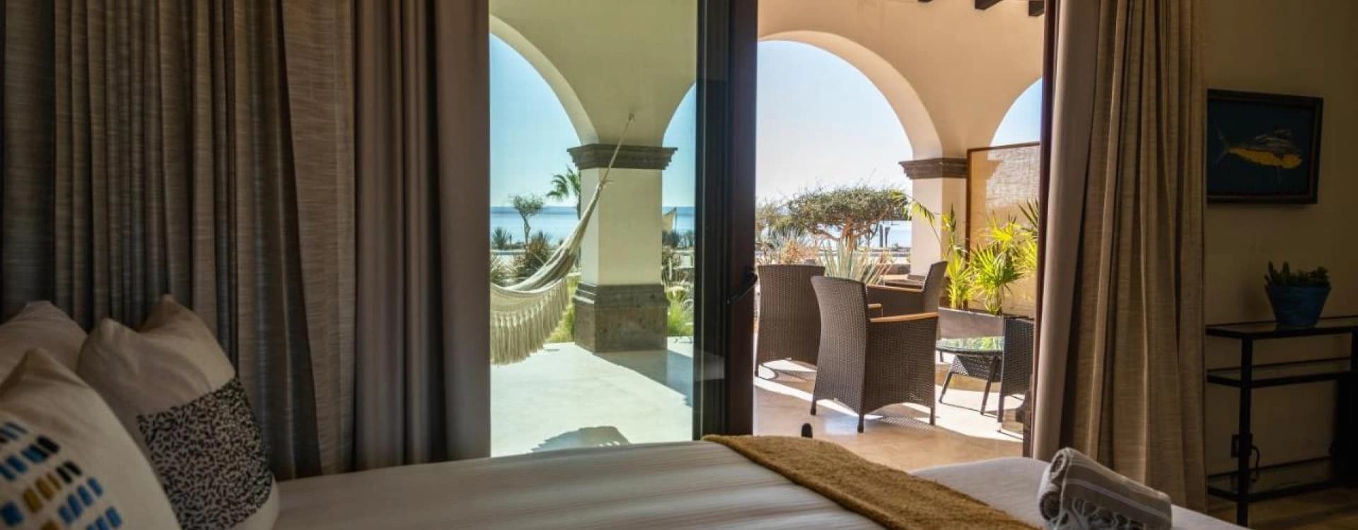Bedroom with a bed facing the open arches of the patio and the hammock