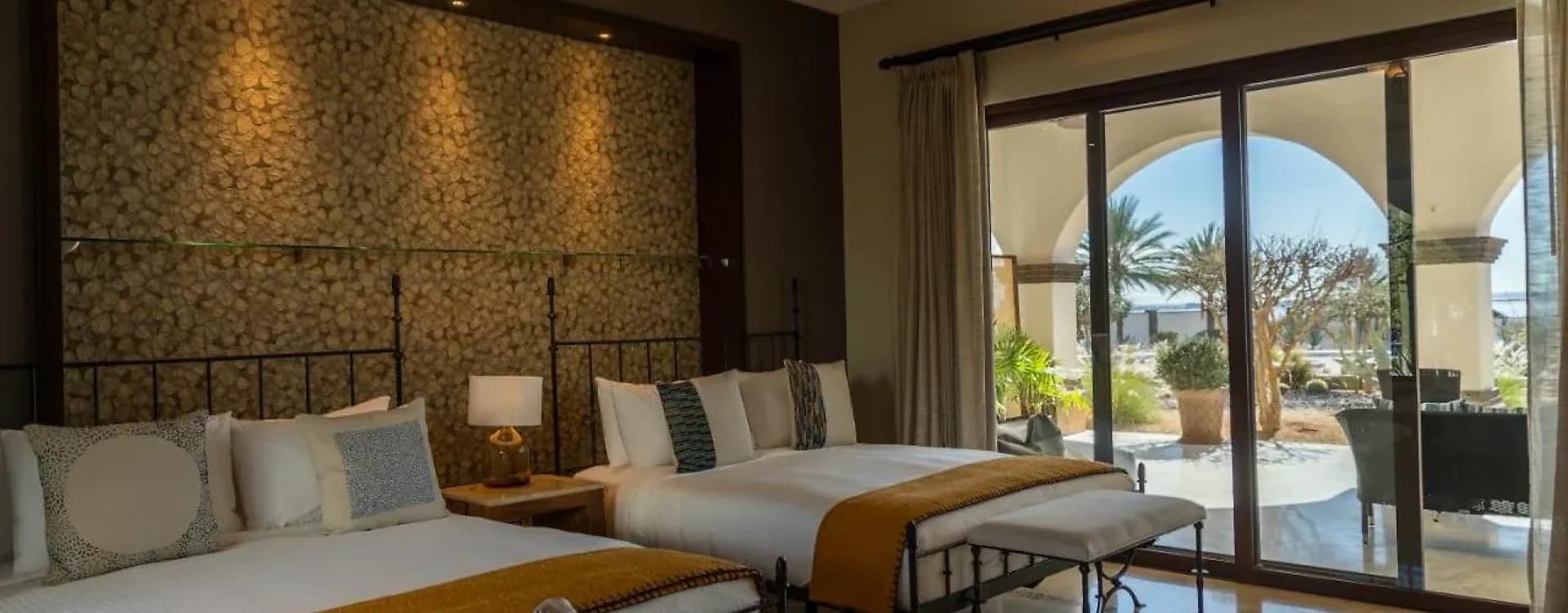 Bed with a bench at the foot, a stone wall and sliding doors onto the patio