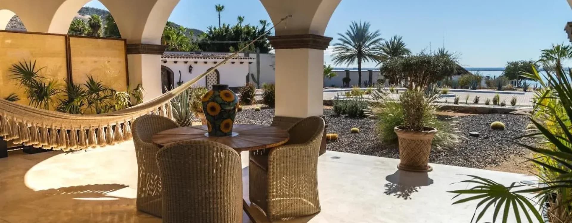 Patio con mesa y sillones de mimbre bajo arcos y vigas de madera