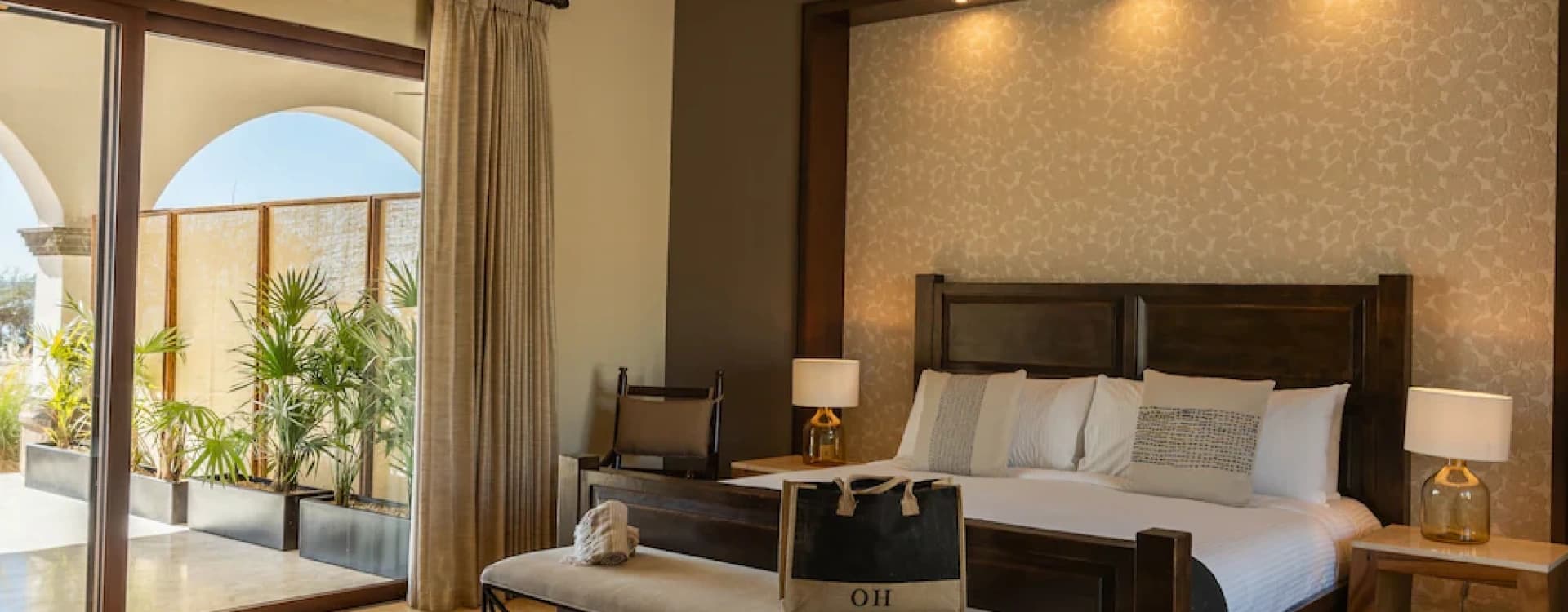 Cama king de madera oscura con banca a los pies y cabecera iluminada