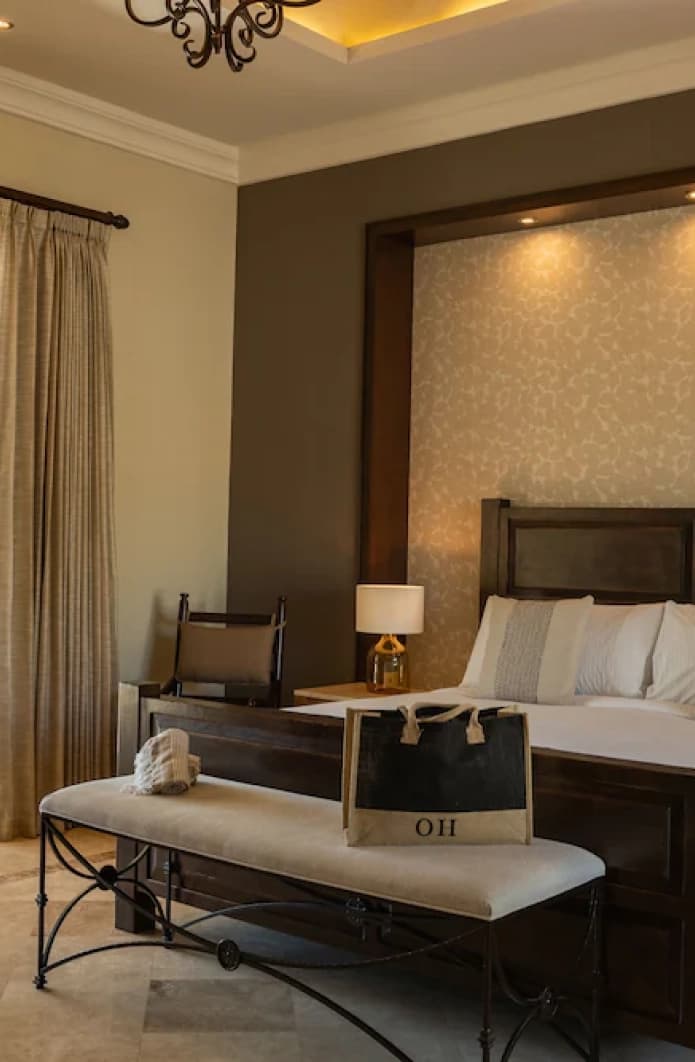 Cama king de madera oscura con banca a los pies y cabecera iluminada