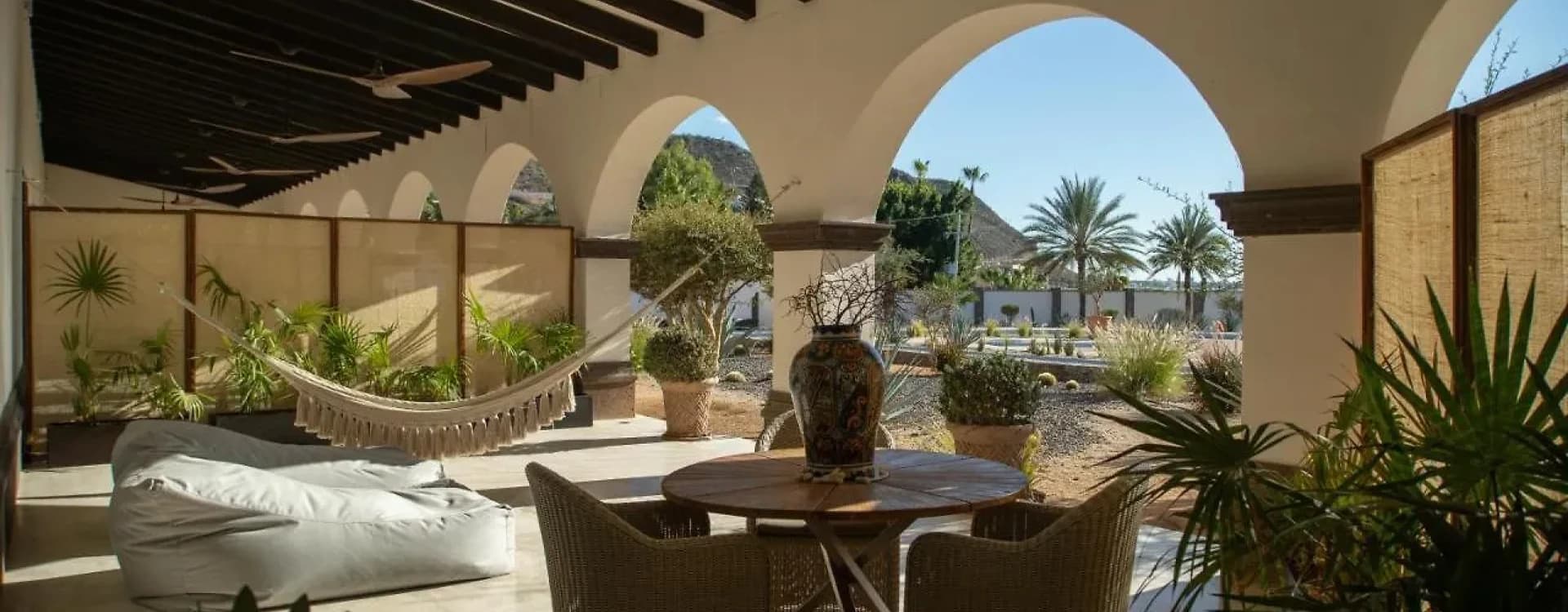Terrace with a hammock, a table and armchairs under arches and timber beams