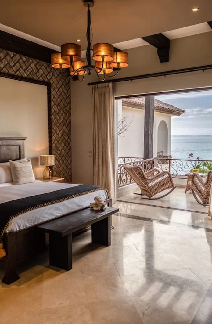 Dark timber king bed with a chandelier, and a balcony with rocking chairs beyond