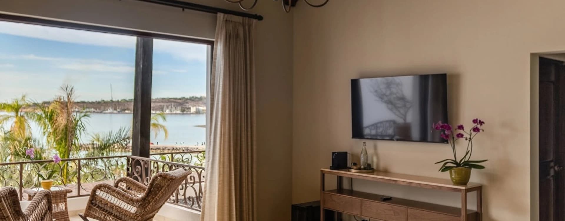 Recámara con candil, mueble con televisión y ventanal con vista al mar