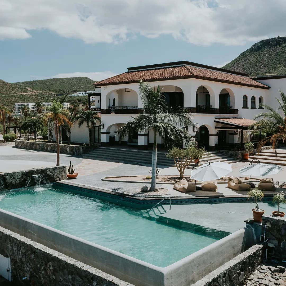 The red-tiled house with white arcades above the turquoise pool, with palm trees and the hill behind