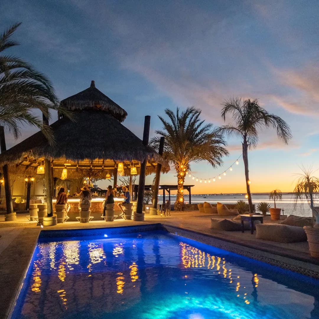 The palapa bar at dusk, with the lit pool and palm trees facing the sea