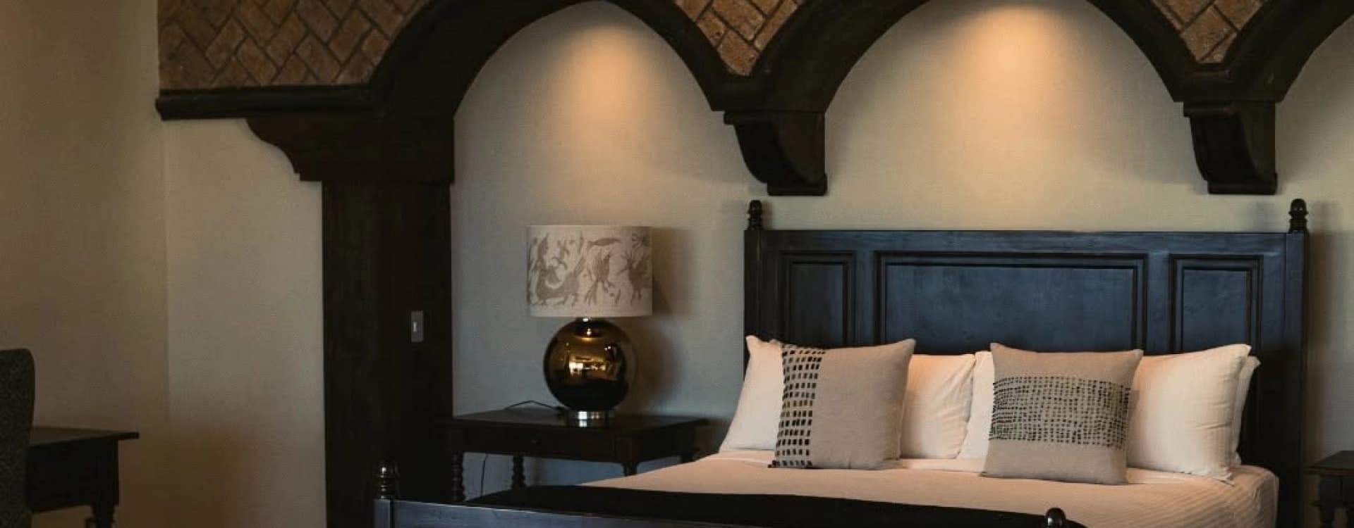 Bed with an arched timber headboard under a herringbone brick wall