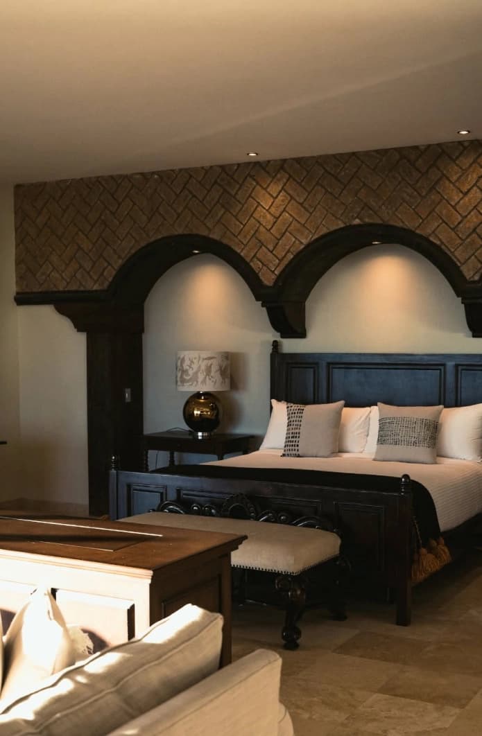 Cama con cabecera de arcos de madera bajo un muro de ladrillo en espina de pez