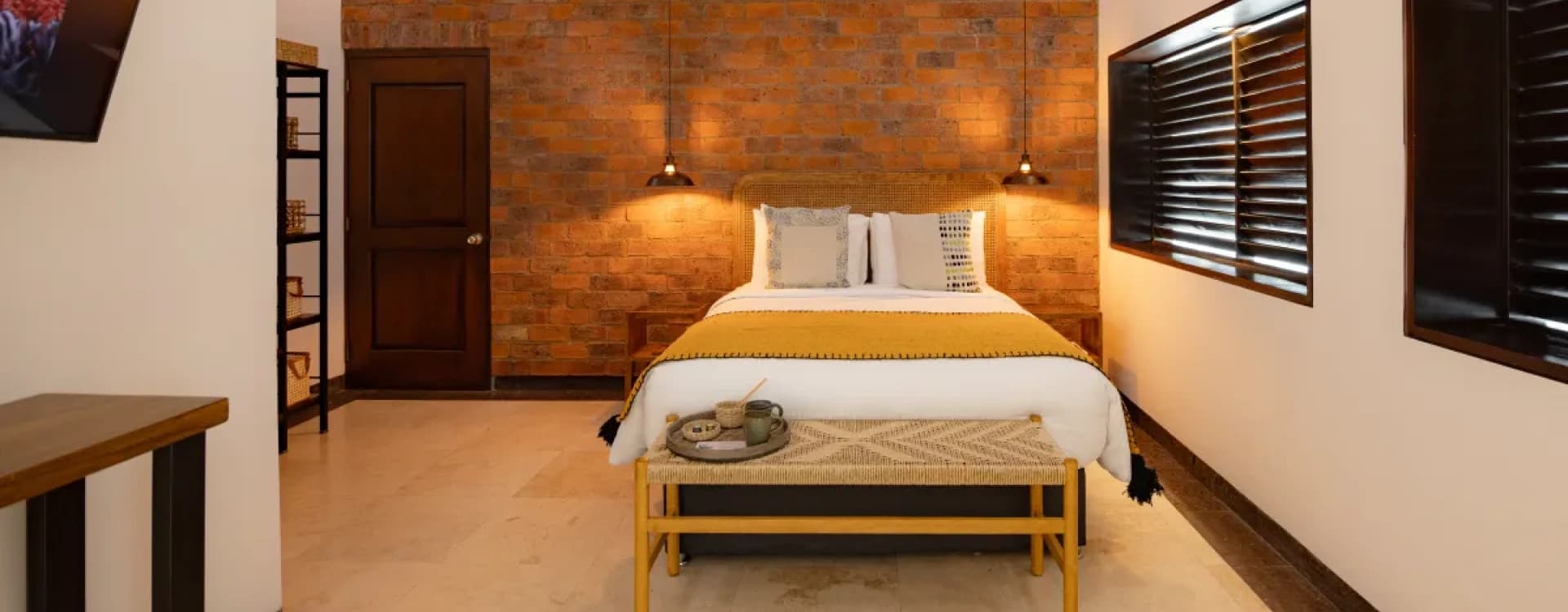 Bed with a bench at the foot under a brick wall and pendant lamps