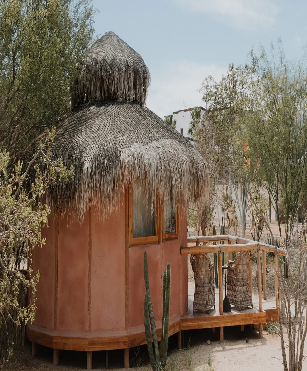 Una de las Botanic Bungalows: cabaña redonda de madera y palapa, con terraza y sillones de mimbre